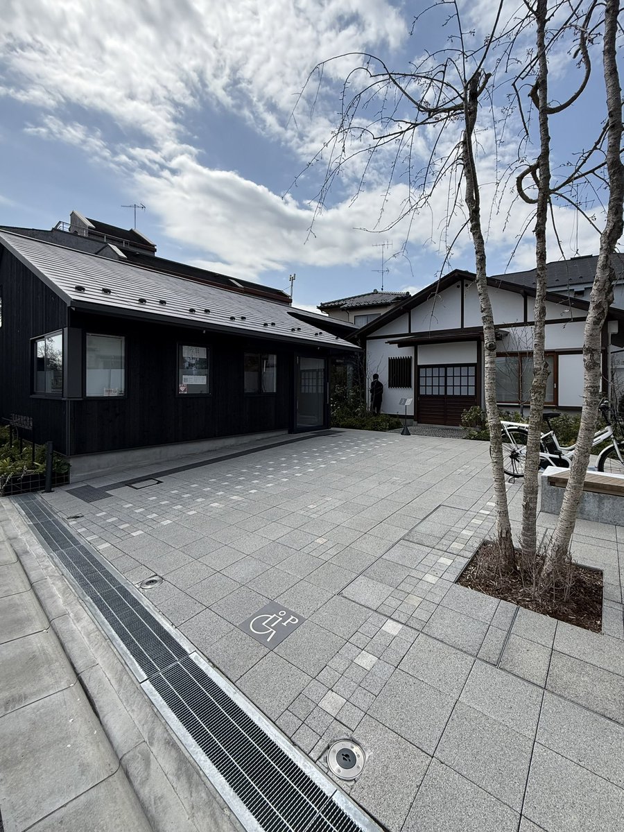 remgoto's tweet photo. 前から行きたいと思っていた、SALHAUSさん設計の「三鷹市吉村昭書斎」に行ってきた。@Arch_Hino 

京王井の頭線、井の頭公園駅より徒歩数分の場所にある。

この地に住んだ作家の吉村昭が書斎にしていた建物を移築して公開している施設。書斎の横に展示スペースのある小さな建築が併設されている。

非常に小さな建築ではあるけれど、建築でしかできないこと、建築にしか出来ないことが具現化されている実感があり、めちゃ良かった！そして、隅々まで考え尽くされている設計にめちゃくちゃ頭が下がる思い、、、。素晴らしい、、、。

道路からは、正面に書斎が見えるように配置して、その横に控えめに受付、展示スペース、トイレなどが入る交流棟が配置されている。

交流棟からは、庭越しに移築された書斎が、色々な方向からぐるりとみわませるようになっていて、またガラス越しに見ると書斎が展示物のようにも見える感覚があり面白い。（庭の植栽は、吉村の旧邸の庭に植えられていたものと同じものが選ばれているとのこと）

交流棟の平面型は、L型で書斎より目立つことを意図的に避けるような形状になっている。そして、書斎の内部に入るためのアプローチ空間にもなっている。

そのような控えめな平面型でありながらも、天井の高さや切妻の天井の形によって、個性は確実に付与されている。その存在感の作り方とバランス感が絶妙で、上手い設計だなぁと感心させられてしまう、、、、！

交流館から一回外に出て、書斎に向かうのだけど、扉の向こう側は天井高の抑えられたクールな空間で、書斎に入るまでの気持ちも整えられる。作家の経歴を紹介する年表もあり、動線空間でありつつも展示空間の一部にしている。上手い。

そして、違う角度からまた庭が見られるのもとても良い。
同じものが色々な角度や違った形で見れるようにするということは体験を重層化させて、豊かにする効果があるんだと思った。

メインの移築された書斎の内観も興味深く。様々な地域の歴史に関する資料がずらっと並んでいる。僕は吉村氏の作品には詳しくないのだけれど、膨大な資料でのリサーチをベースに小説を書いていたことが伝わり、ジャンルは違うけどもプロフェッショナルの在り方が実感できた。

エントランスの広場は、障がいを持った型向けの駐車場も兼ねているのだけれど、一体型の広場にも使えるような作りとしていたり、脇のベンチもコンクリートに木製ベンチを埋め込むようなデザインにしていたりと、本当に細やかに設計がされていて、体験的な気持ちよさと、建築的発見の知的な快感が同時にくるような感じ。

社会的に開かれていると同時に建築的にも突き詰めようとしているというか。

吉祥寺方面に来られる方には、ぜひ寄ってもらい建築だと思った、、、！内覧会には伺えなかったので、やっと宿題を終えた気分、、、、！

皆様ぜひ！