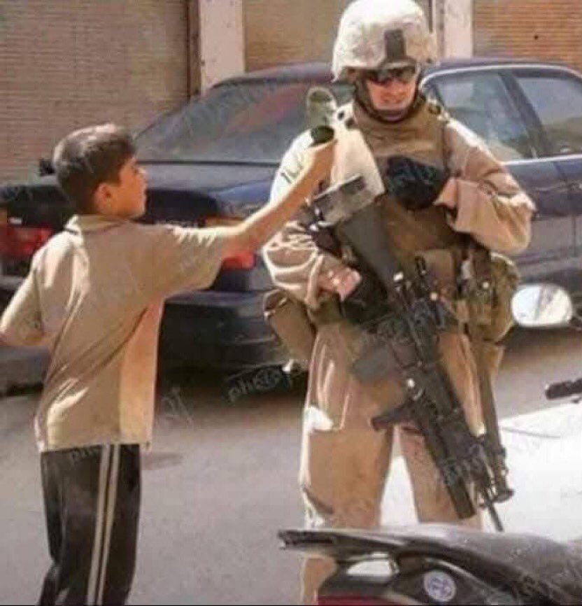 umtikrit's tweet photo. طفل سُني عراقي يرفع حدْاءه بوجه جندي من القوات الامريكية!

والله أن الحدْاء الذي في يد الطفل لأطهر من السيستاني وجميع المراجع. https://t.co/esnBhSXCF2