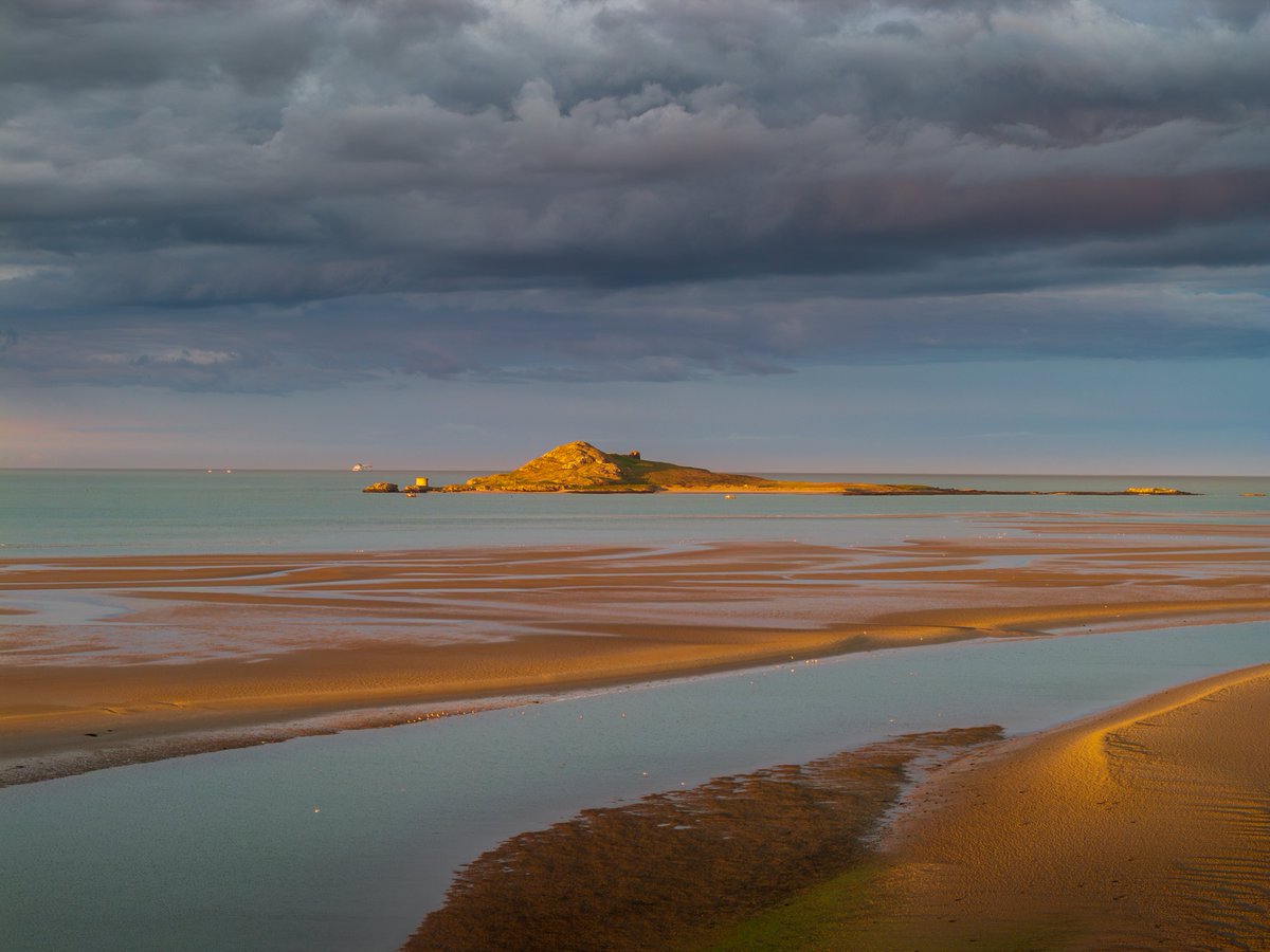 Golden hour light reflecting on Ireland's Eye with a moody sky above at sunset.