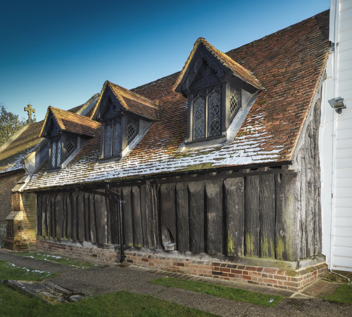 A photograph of the exterior of the side wall of a wooden church with 3 dormer windows in the roof.