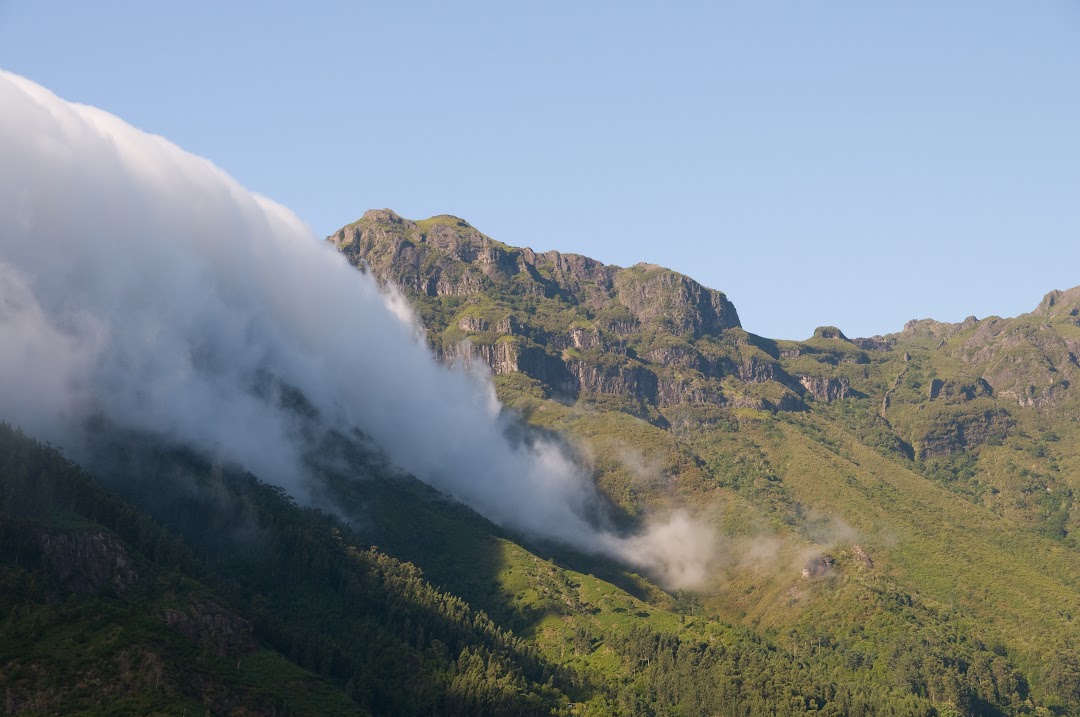 Madeira's tweet photo. #Madeira 

The mountains of Madeira play a key role in what’s known as the orographic effect. When moist air from the ocean is pushed upward by the island's steep slopes, it cools rapidly, leading to condensation and the formation of clouds. This is why you often see clouds hanging low over the mountains, as depicted in the X post image where a thick layer of fog or cloud is seen rolling over the peaks. The web result mentions how the mountains, often rising above 1,400 meters, "block the gusts and clouds," causing them to accumulate on the windward side, particularly in the north.