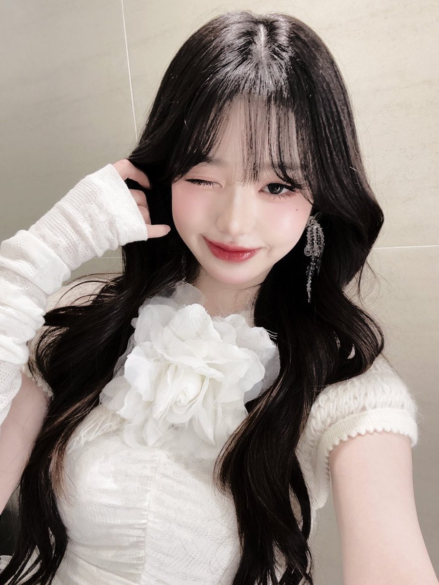 A   bloom,  a   whisper  of   spring’s   hesitant
awakening, rests  upon  her  collar, its petals   
unfurl   in   delicate   defiance,  mirroring  the 
mischievous    poetry   that   dances   in   the 
mischievous glint  of her  eyes  as she winks