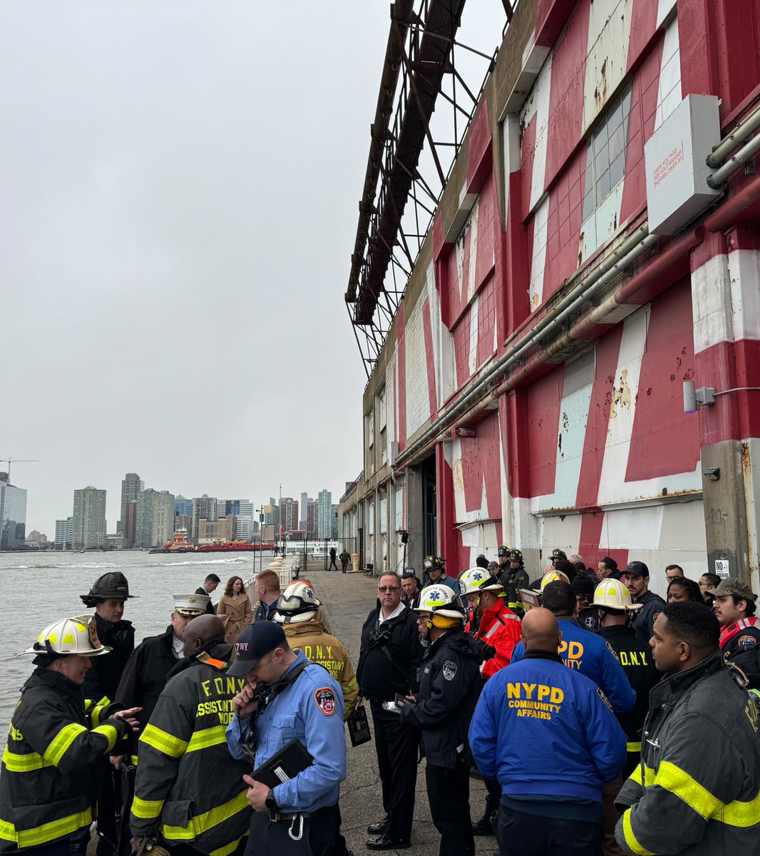 Scene at pier where several first responders are standing, first responders in water in distance