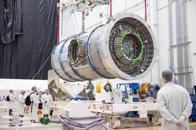 Inside Northrop Grumman’s facility in Gilbert, Arizona, Gateway’s HALO module is suspended in midair by a crane as technicians in cleanroom garments observe the operation. The cylindrical metallic module features docking interfaces with alignment markings. Surrounding the module is specialized handling equipment used to support its movement. Credit: NASA/Josh Valcarcel