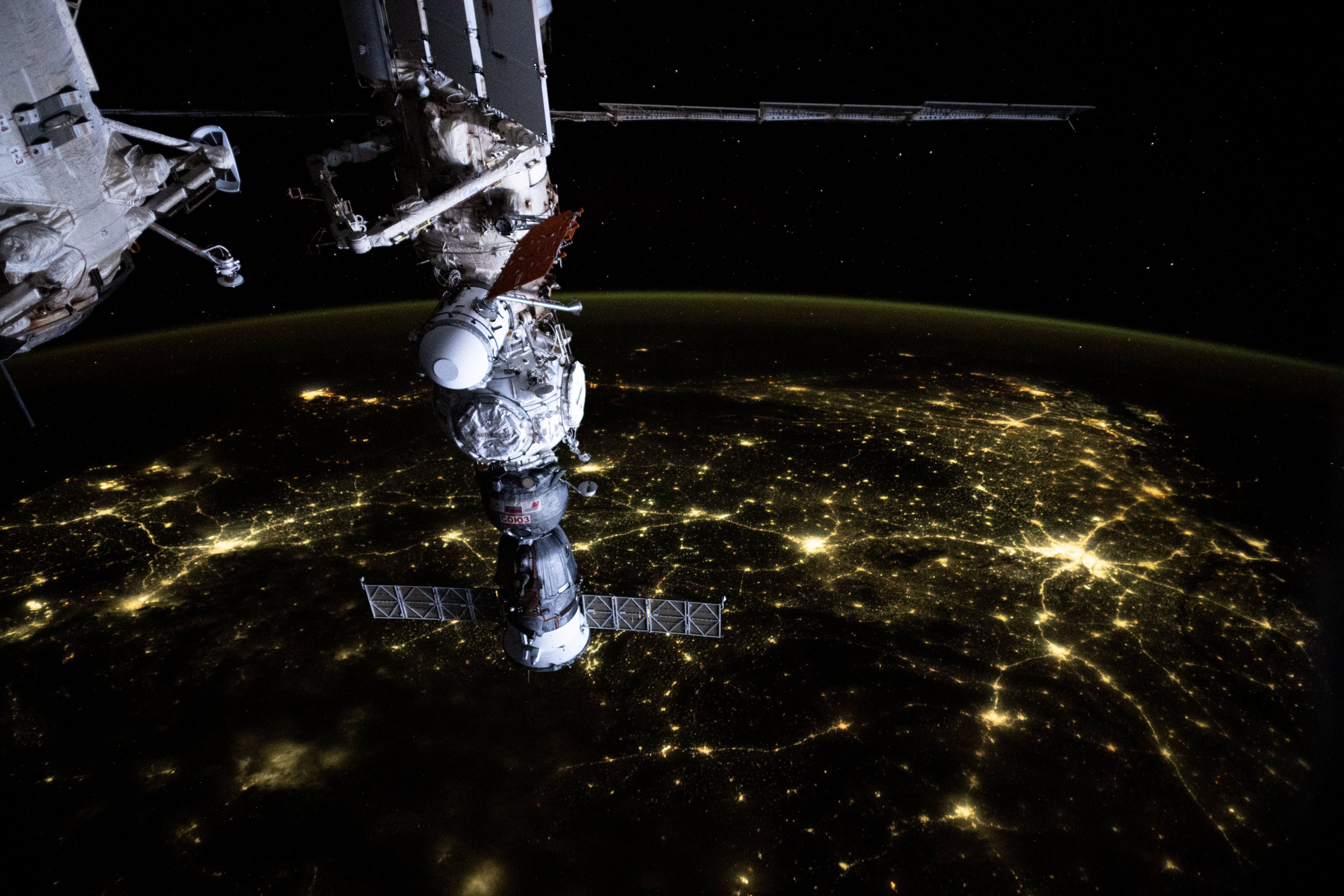 iss071e074030 (May 14, 2024) --- An atmosphreric glow blankets Earth's horizon and a web of city lights interconnect across India in this photograph from the International Space Station as it soared 256 miles above the subcontinent. In the foreground, the Soyuz MS-25 crew ship is pictured docked to the Prichal docking module which is itself attached to the Nauka science module.