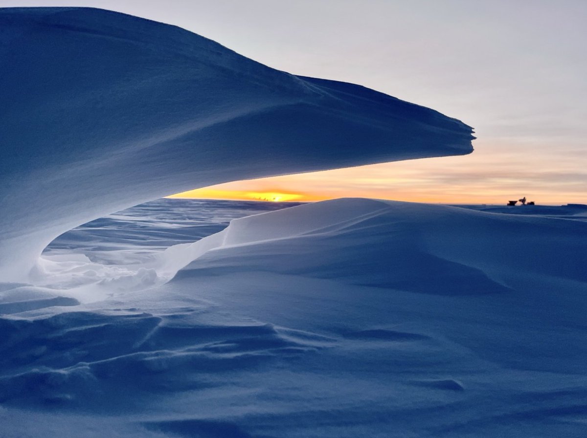 Picture by <a href="/NOAA/">NOAA</a> winterover Ian Crocker, of a drifting sastrugi wave, with the #sunset behind the ceremonial #southpole and the profile of the SPT and dark sector telescopes in the distance on the right.