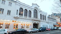 merlinpapin3's tweet photo. .@FredOL69007 @tbarnaud Aujourd’hui, dans le cadre des Cinémas de Quartier qui ont forgé ma cinéphilie, je voudrais vous parler d’un lieu mythique de Paris : #LeTrianon.
Situé boulevard de Rochechouart, à deux pas du métro Anvers, le Trianon est aujourd’hui classé à l’inventaire des Monuments Historiques. Mais pour moi, il représente avant tout un moment de vie, un lieu que je fréquentais assidûment lorsqu’il était encore exploité comme salle de cinéma.
Il y avait alors une drôle de proximité avec l’Élysée Montmartre, haut lieu du catch français dans les années 60-70. Aujourd’hui, cette partie de Paris attire une jeunesse branchée, avide de concerts (Indochine, BB Brunes, Stromae), de spectacles modernes et de stand-up. Mais il fut un temps où l’ambiance était toute autre.
Le Trianon voit le jour en 1894, conçu comme un théâtre à l’italienne, avec ses deux balcons, ses hauts plafonds et ses piliers qui couraient tout au long de la salle. Il pouvait accueillir près de 1 000 personnes, dans une configuration large et profonde, à mille lieues des “cages à lapins” que nous imposent certains multiplexes actuels.
Il s’appelait à l’origine Trianon-Concert, avant de changer plusieurs fois de nom. Un incendie majeur l’endommagea, ainsi qu’une partie de son voisinage, mais il fut reconstruit et rouvrit ses portes en 1902. Avant la Première Guerre mondiale, il se spécialisa dans le music-hall avec des artistes comme Fréhel, Guibert ou Pierre Dac.
Puis, pendant plus de 40 ans, ce fut un cinéma. Un des plus réputés de la capitale. Sa proximité avec Pigalle et les pentes de Montmartre attirait un public nombreux, qui appréciait la grandeur de la salle et son immense écran. Dans son agencement à deux balcons, il évoquait le Grand Rex, bien que dans une autre ambiance. Escaliers et coursives y ajoutaient une vraie majesté.
Moi, je l’ai connu dans les années 70, quand je suis arrivé dans le quartier avec ma mère et mon frère. Ma mère venait de s’y installer, et quelle chance : une dizaine de cinémas autour de la maison ! Une autre époque. Une faune colorée, bon enfant, entre la place Clichy et Barbès, avec tous ces cinémas alignés presque du même côté de la rue, très fréquentés par des jeunes comme moi.
Au Trianon, on voyait beaucoup de films d’aventure. Pas des avant-premières, non, mais peu importait. Le cinéma s’était spécialisé dans les films de kung-fu, alors en plein essor, et que l’on découvrait avec les yeux écarquillés. Comme on avait découvert les westerns spaghetti quelques années plus tôt. Bruce Lee, Franco Nero, Terence Hill, Bud Spencer... c’était du vrai cinéma de quartier. Pas besoin de réfléchir, juste vibrer.
Pas des chefs-d’œuvre, d’accord. Mais combien d’acteurs devenus célèbres ensuite y avons-nous découverts ? Clint Eastwood, Charles Bronson, Lee Van Cleef… Tous passaient par là, par ce grand écran un peu fatigué, mais fidèle.
Une petite part de ma passion pour le cinéma s’est construite là, dans cette salle populaire, dans cette ambiance unique. C’était un lieu d’évasion, un peu magique, un peu brut.
Au milieu des années 80, le Trianon ferma comme tant d’autres salles alentour. Mais lui, il eut la chance de ne pas devenir un multiplexe. Il conserva ses dorures, ses balcons, ses volumes. Et lorsqu’il fut racheté, on en fit un des hauts lieux de la culture parisienne : concerts, spectacles, événements… Il rejoignit alors cette constellation de lieux emblématiques comme l’Élysée Montmartre, la Cigale ou le Divan du Monde.