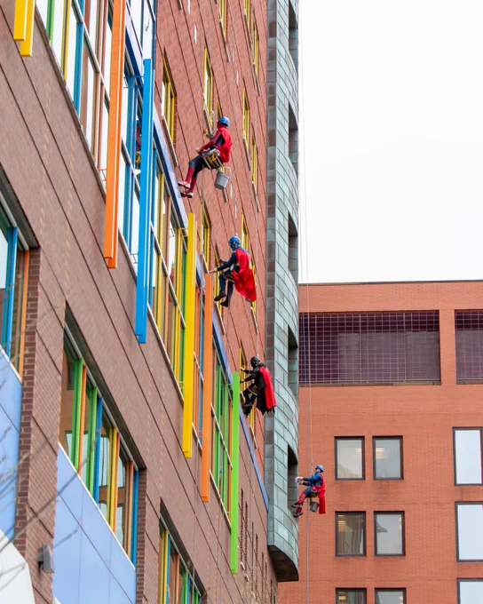 Several individuals are rappelling down the colorful facade of a multi-story building during a public event.
