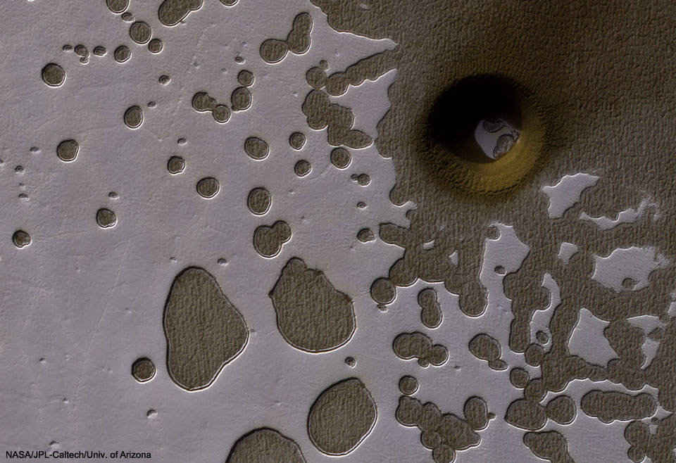 What created this unusual hole in Mars? Actually, there are numerous holes pictured in this Swiss cheese-like landscape, with all-but-one of them showing a dusty, dark, Martian terrain beneath evaporating, light, carbon dioxide ice. The most unusual hole is on the upper right,