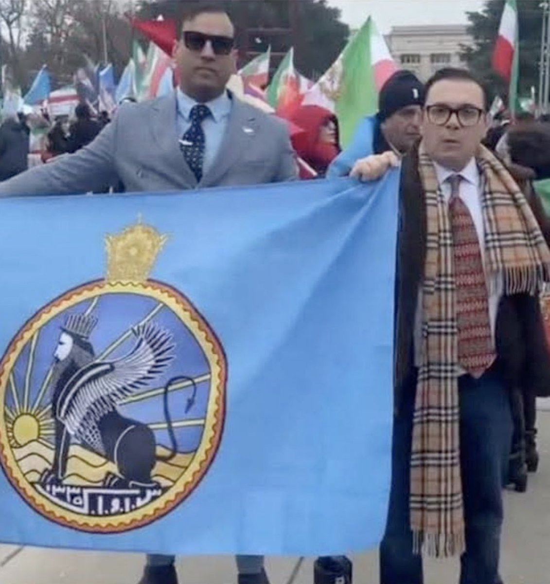 Shahram Makoui (right), the chief organizer of the poorly attended rally, is seen holding a SAVAK flag—a symbol of the deposed monarchy whose brutal secret police were notorious for torture and repression, as documented by Amnesty International and The New York Times.