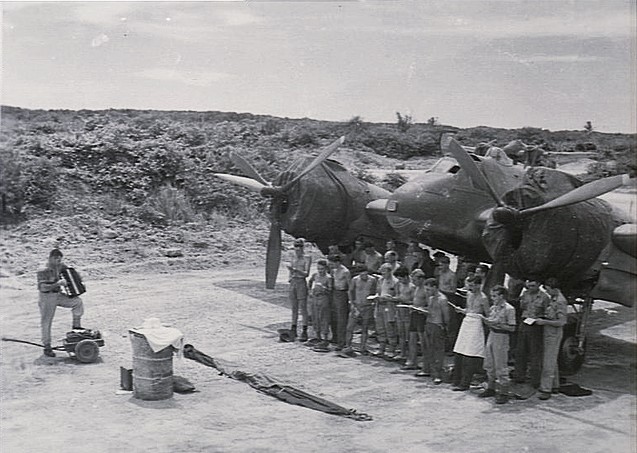 DWB55's tweet image. Kiriwina Island
Trobriand Islands
Solomon Sea.
Off the north coast of Papua New Guinea:
On a sultry, humid tropical 1944 Easter Sunday morning, the chaplain of No 30 (Beaufighters) Squadron, Flt Lt Hardie, leads the hymn singing with his accordion.
The oil drum used as an altar.