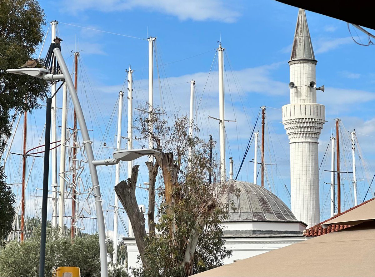 İki Dünyanın Kesiştiği Yerde: Bodrum'da Minare ve Yelkenler

Caminin beyaz minaresi, beyaz yelken direkleri arasında - bir nevi şehrin iki farklı yüzünün tek karede buluşması. Karşımda, birbirinden tamamen farklı iki yaşam biçimini temsil eden yapılar, şaşırtıcı bir uyumla yan