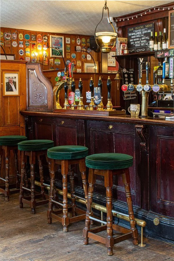 Britains___Pubs's tweet photo. A bar stool is called a bar stool because it's supposed to be.... at the bar. Real pubs support the age old custom of drinking at the bar itself, whilst gastro environments prefer you to sit at tables like it's a restaurant. Look out for pubs with real barstools and the metal bars that run along the bottom for people to rest their feet.
