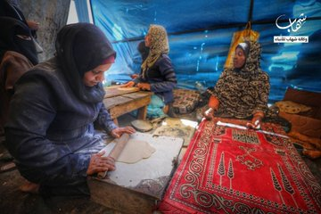 Palestinian women bake bread for residents of Al-Nuseirat camp despite all hardships, amid the rubble of their home destroyed by the Israeli aggression.