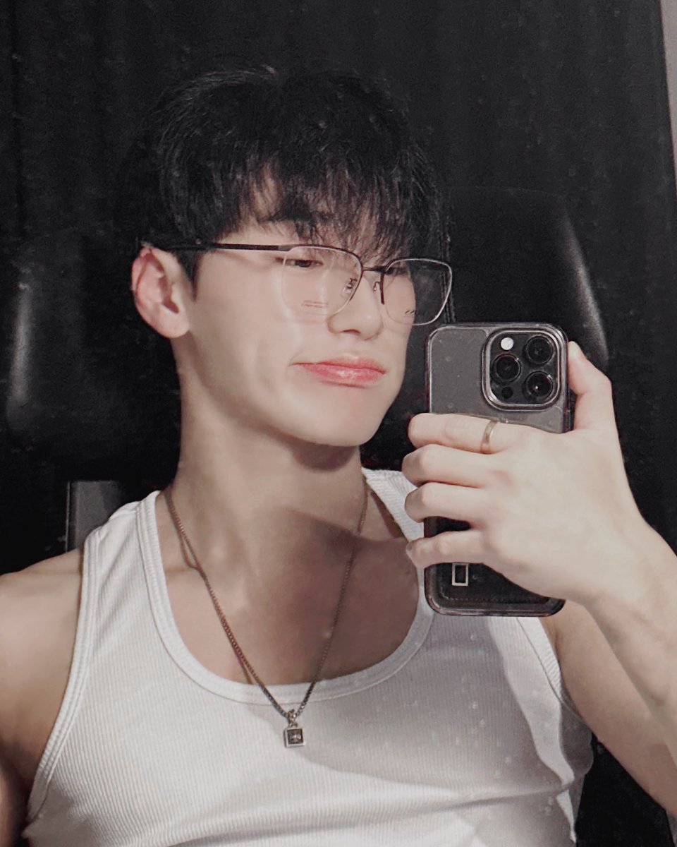 Snapping a sleek mirror selfie with my smartphone, rocking stylish glasses and a bold gold ring, set against a moody dark backdrop.