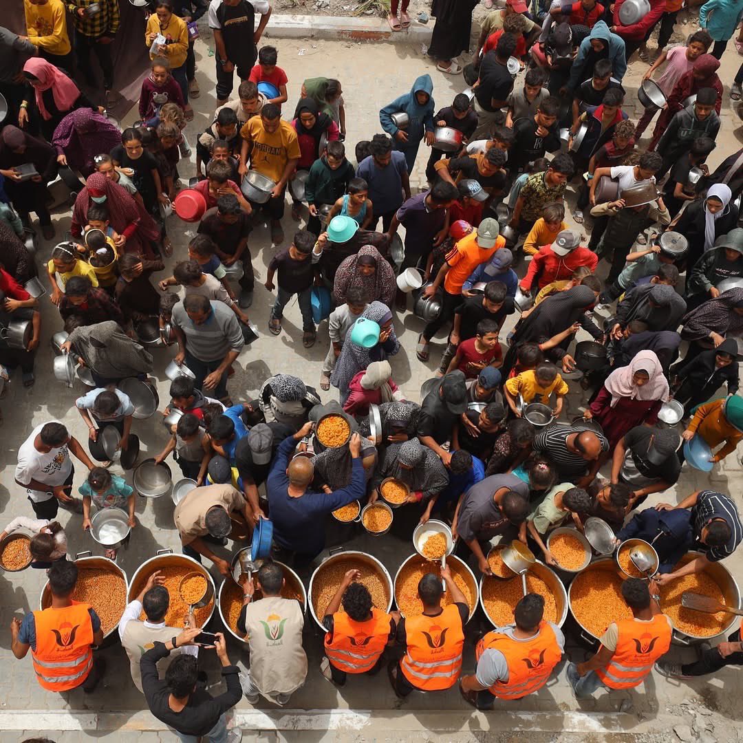 Displaced children queue with their pots to receive food aid from a relief kitchen near a police station-turned-shelter in Gaza City, amid dire humanitarian conditions.
