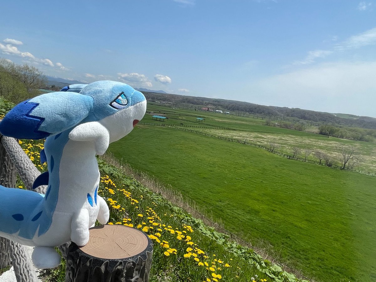 Palworld Chillet plush sitting in the lush green fields of Hokkaido, Japan with beautiful natural scenery in the background