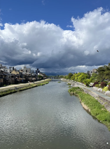 ！静かに流れる川、川沿いの豊かな緑、遠くの自然と溶け合う街並み、そして空に漂う雲は、まるで人生の静けさと美しさを物語っているかのようです。