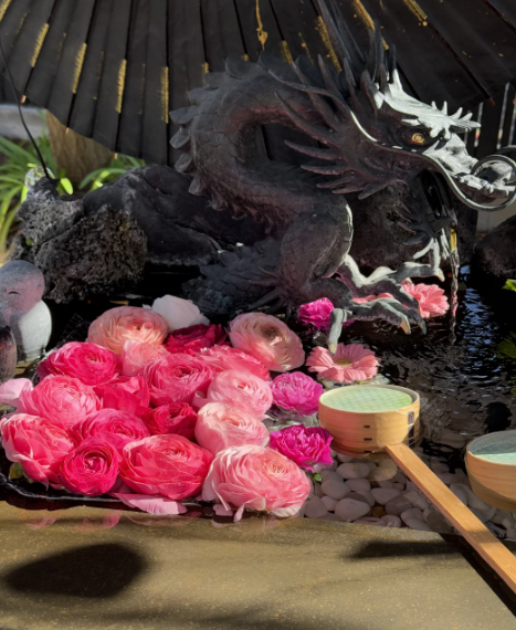 黒龍の彫刻は満開のピンクの花の海の中に陣取っていて、水面は光と影を映し出しています。そばには伝統的な木のスプーンや水鉢もあり、禅と東洋の趣が満ちています
