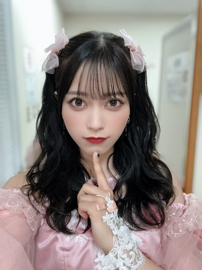 The image features a person dressed in a pink, lace-trimmed outfit, which is styled in a kawaii (cute) fashion. The individual has long, wavy black hair adorned with pink bows, enhancing the cute aesthetic. The setting appears to be indoors, possibly in a hallway or a room with posters on the walls. The post text 'kawaii🎀？' suggests that the person is showcasing their cute and fashionable appearance, likely aiming to evoke a sense of charm and playfulness. The overall composition is bright and cheerful, fitting the theme of fashion and beauty.