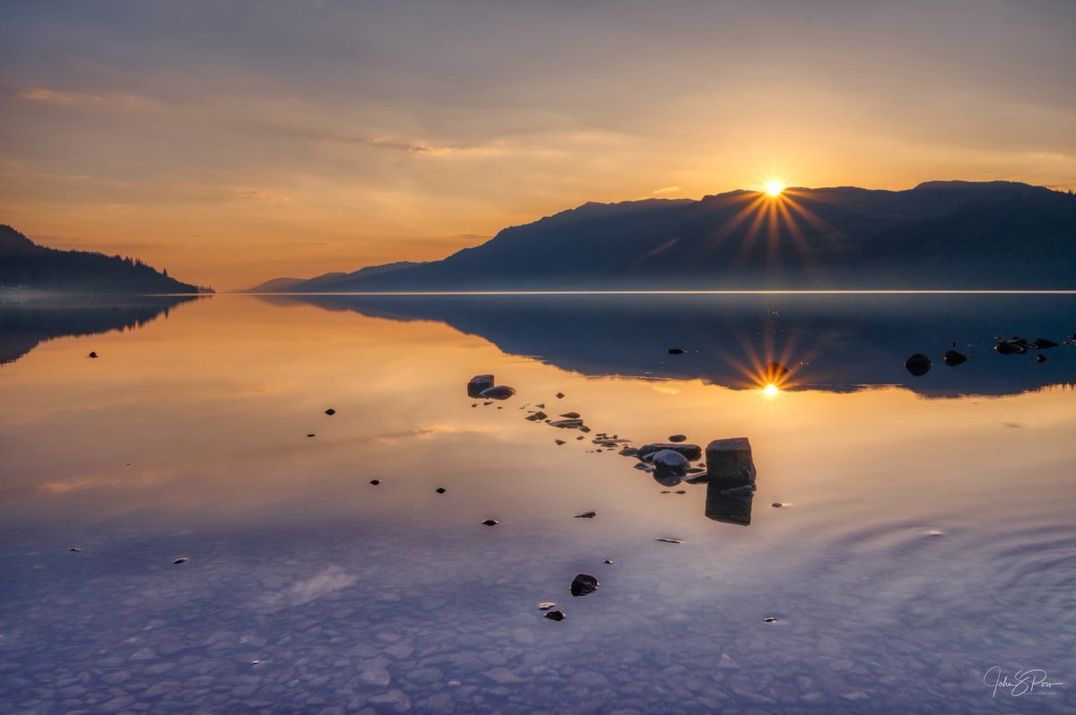 Sunrise at Loch Ness, with a reflected starburst.  

I could say that the Loch Ness Monster is just out of frame causing the ripple, but that was a duck 🦆.