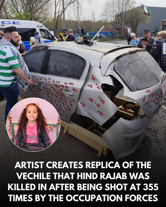 The image shows a detailed replica of a car that was involved in the tragic incident where Hind Rajab was killed. The car is displayed outdoors, surrounded by people, possibly at a public event or exhibition. The vehicle is heavily damaged, with numerous red marks indicating bullet holes, signifying the violence it endured. An inset photo of a young girl, presumably Hind Rajab, is included in the image, adding a personal touch to the memorial. The text overlay at the bottom of the image reads, "ARTIST CREATES REPLICA OF THE VEHICLE THAT HIND RAJAB WAS KILLED IN AFTER BEING SHOT AT 355 TIMES BY THE OCCUPATION FORCES," providing context to the artwork's purpose. The post text from WearThePeace (@WearThePeaceCo) further explains that the artist created this replica to educate people about Hind Rajab's story.