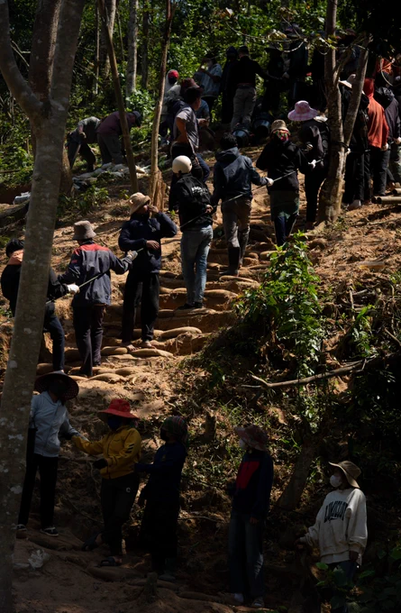 A line of people along a hillside passes items up and down.