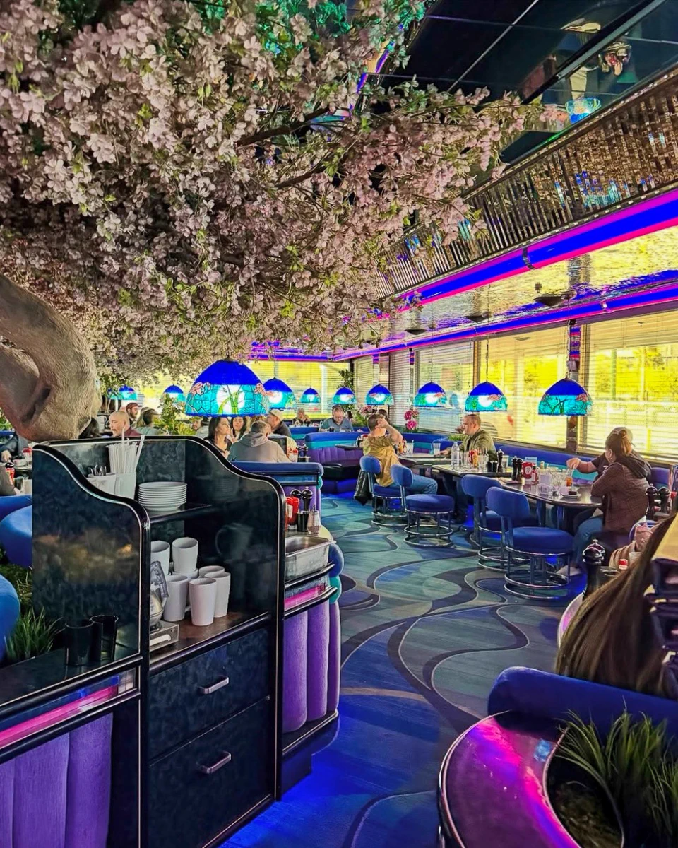 Interior, showing patrons seated at tables under lamps. The decor features vibrant blue lights and abundant cherry blossoms.