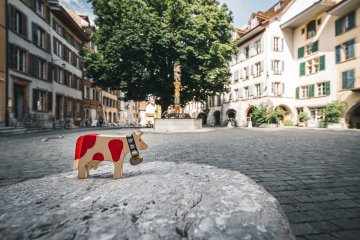 Can you guess where I'm moo-ving today? 🐮🇨🇭

Here are two clues from my latest stop:
⌚ This city is world-famous for its watchmaking know-how — even my tail started wagging on time!
🌊 It sits by a beautiful lake, with the Jura mountains watching over.

Any ideas where I am? 👇