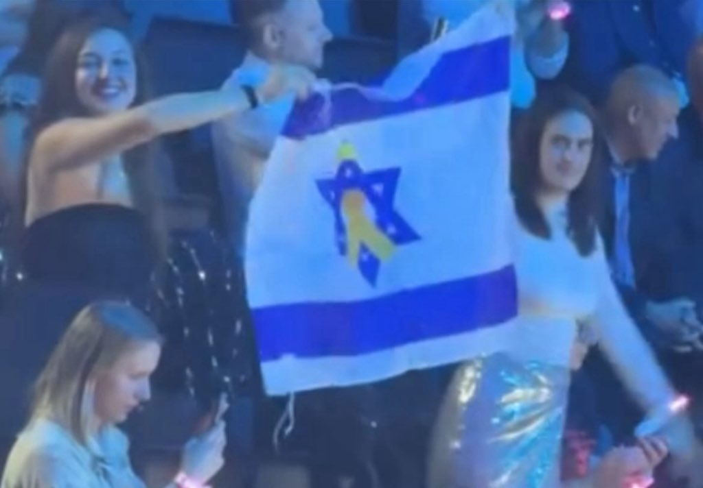הדגל הכי מרגש בבאזל: הילה, אחות של לוטן אביר ז״ל שנרצח במיגונית שבה שרדה יובל ב-7.10 מניפה את דגל ישראל עם עיטור החטופים בגאון באירוויזיון