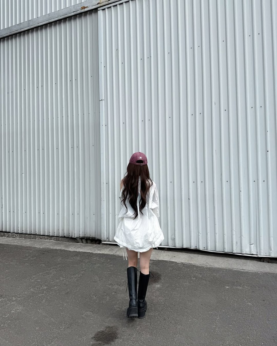 Boots on concrete, jacket slipping off her shoulder like a whisper. With each step, she leaves behind a little bit of silence, framed by the steel-gray backdrop that makes her softness stand out even louder.