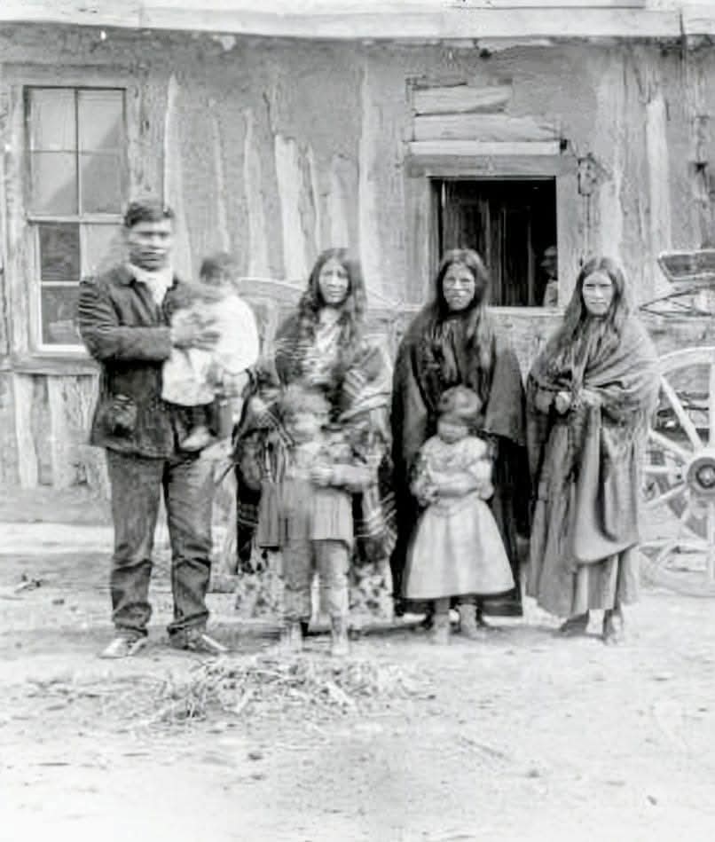 This photograph, taken in Colorado around 1900, captures an unidentified Native American family standing in front of their cabin home. The image offers a rare glimpse into the everyday lives of Indigenous families during this time, highlighting the contrast between traditional