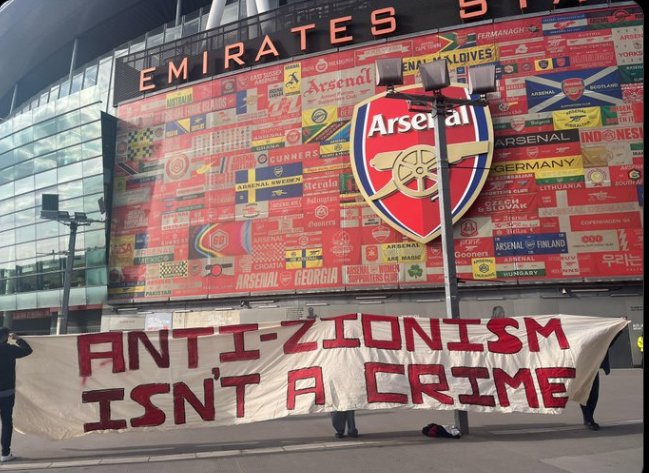 Fans of <a href="/Arsenal/">Arsenal</a> display two banners outside the Emirates Stadium, London, to show the red card and support for Mark Bonnick.

Mark was shamefully sacked by Arsenal for criticising Zionism on X, after working for the club for over 20 years.