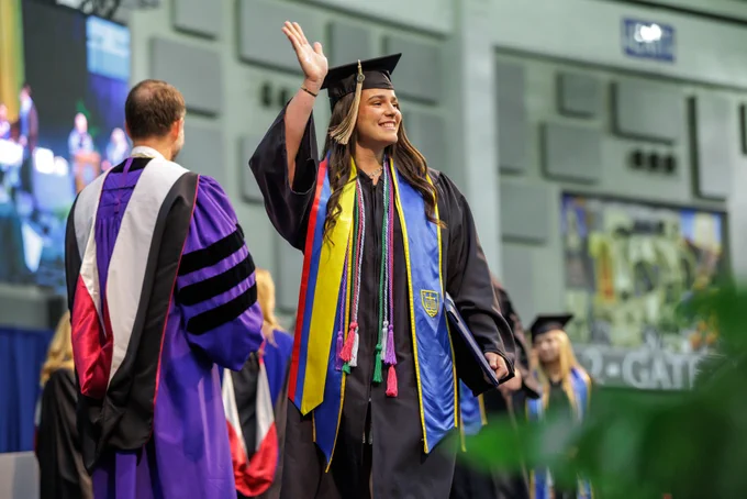 A Notre Dame Mendoza graduate walks across the stage at the diploma ceremony and waves to the crowd. 