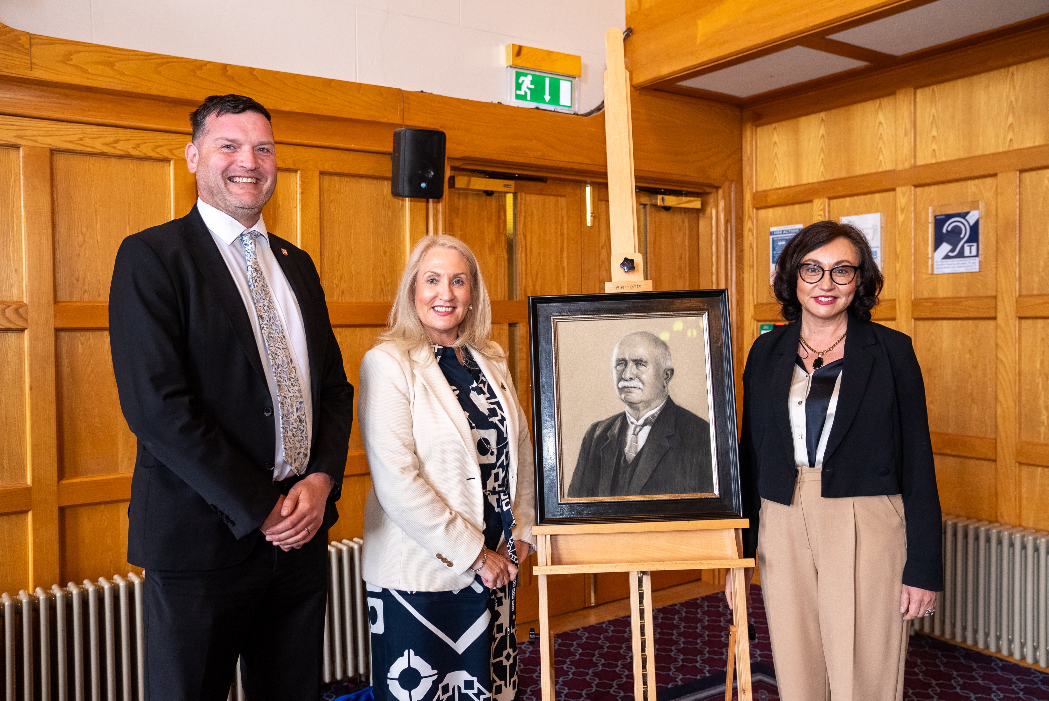 Alistair Stewart (Queen's University Belfast) and Honorary Consul Caroline Keenan stand on left side of portrait of William Ferguson Massey and New Zealand Acting High Commissioner Guergana Guermanoff stands to the right