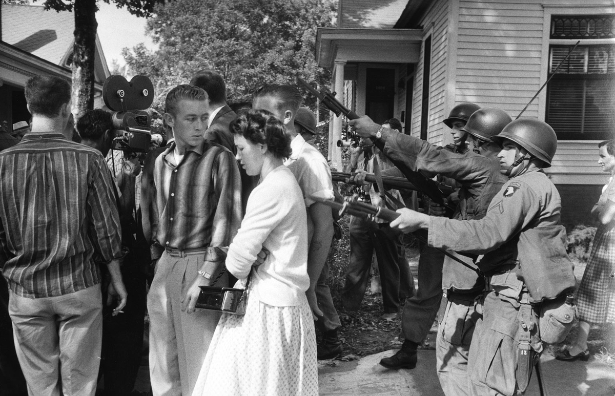WomanDefiner's tweet photo. I just want to point out something real quick. The same people throwing a fit about non citizens being detained and deported, celebrate acts like the one shown below where state agents pointed guns at kids and parents because they didn't want to go to school with other people.

They were fine using violence to take people's freedom of association away.