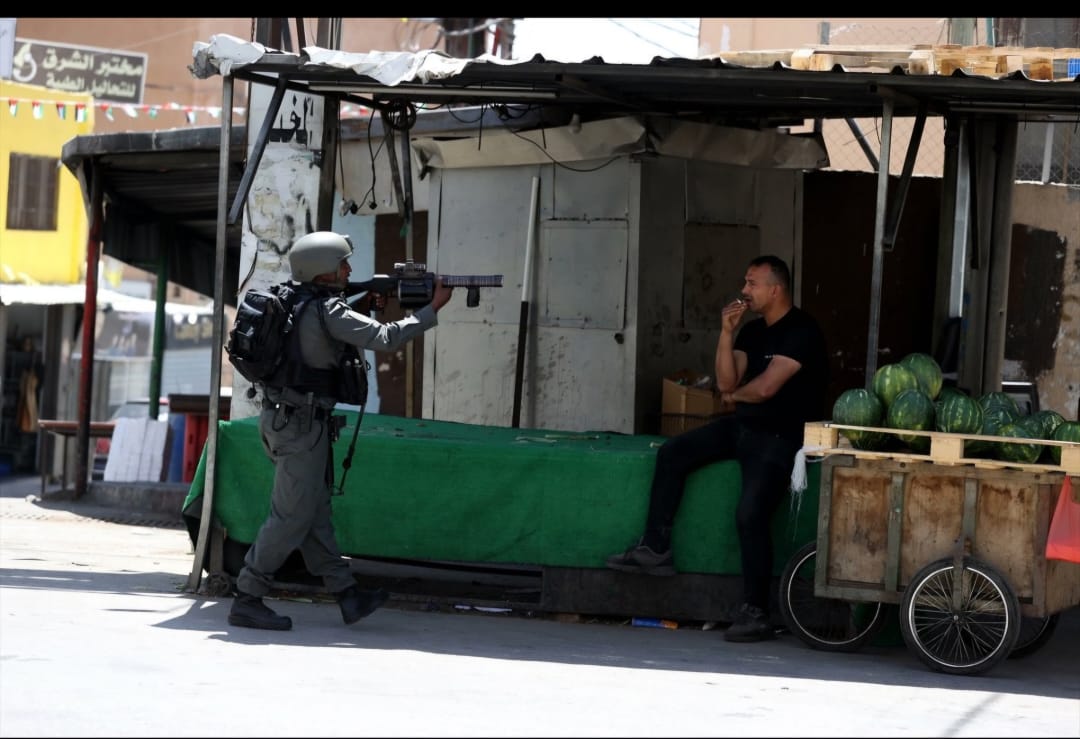 Toute la cause palestinienne en une photo prise à Naplouse en Cisjordanie. Le soldat israélien lâchement armé jusqu'au dents qui menace un palestinien qui fume sa cigarette à côté d'un stand de pastèques, devenu un de nos symboles. Notre patience, notre sang froid, notre courage,