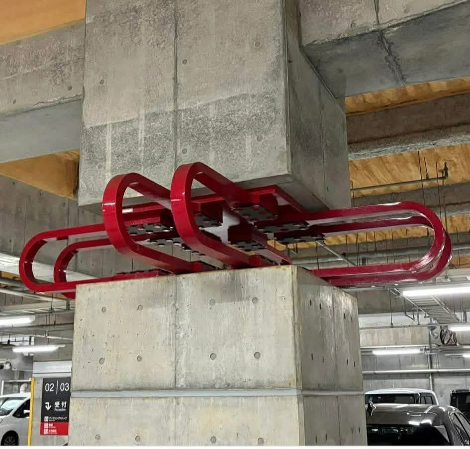 dnahinga's tweet photo. The image shows a structural engineering solution used in a building in Miyazaki, Japan, to mitigate earthquake damage. 

The concrete pillars supporting the building rest on red, curved metal structures, which act as shock absorbers. Here's how it works:

1. Base Isolation: The metal structures are part of a base isolation system. They allow the building to move independently of the ground during an earthquake, reducing the transfer of seismic energy to the upper parts of the building.

2. Shock Absorption: The curved metal components are likely made of a material like steel, designed to deform and absorb energy. When the ground shakes, these structures flex, dissipating the earthquake's energy as heat and movement, rather than letting it travel directly into the building.

3. Stability Maintenance: By absorbing and dissipating the seismic forces, the system keeps the upper parts of the building relatively stable, minimizing structural damage and protecting occupants.

This design is a common earthquake-resistant technique in seismically active regions like Japan, ensuring buildings can withstand tremors while remaining intact.

🏘️🏡✅