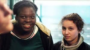 merlinpapin3's tweet photo. .@FredOL69007 #DéfiCinéClassique2025 Mai (Caméra d’Or 2016) Vu le film #Divines de Houda Benyamina (2016) avec Oulaya Amamra Déborah Lukumuena Jiska Lavanka Kevin Mischel Yasin Houicha Farid Larbi Madjouline Idrissi Mounir Margoum
En banlieue parisienne, la jeune Dounia a soif de pouvoir et de réussite. Soutenue par sa meilleure amie Maimouna, elle abandonne le lycée professionnel et propose ses services à Rebecca, une dealeuse respectée dont elle gagne progressivement l'estime. Sa rencontre imprévue avec Djigui, danseur troublant de sensualité, va l'ébranler, mais il est difficile de sortir de l'emprise de Rebecca.
Il y a dans Divines une rage, une impétuosité, un souffle vital qui emporte tout sur son passage – à commencer par les maladresses du scénario ou les outrances de ton. Premier long-métrage de Houda Benyamina, le film a fait irruption au Festival de Cannes comme une gifle, remportant la Caméra d’or, et a confirmé que le cinéma français savait encore accoucher de voix neuves, pas formatées, prêtes à tout bousculer. Avant de sombrer dans les égarements du blockbuster féminisé (Les Trois Mousquetaires), Benyamina signait ici une œuvre âpre, inégale mais furieusement habitée, avec pour trinité explosive un trio de jeunes comédiennes incandescentes : Oulaya Amamra (sa sœur dans la vie), Déborah Lukumuena et Jisca Kalvanda.
L’histoire est simple mais percutante. Dounia (Amamra), ado de cité, vit dans un bidonville en marge d’une banlieue parisienne, avec une mère paumée, et n’attend plus rien de l’école. Elle est fascinée par le pouvoir, l’argent, la réussite. Avec sa meilleure amie Maimouna (Lukumuena), elle décide de se lancer dans le deal, épaulée par une caïd locale charismatique, Rebecca (Kalvanda). Dounia croise aussi la route d’un danseur de hip-hop, Djigui (Kevin Mischel), beau et aérien, qui réintroduit une tendresse inattendue dans ce monde de violence. Mais dans cet univers sans filet, la chute est rapide, brutale.
Ce qui frappe d’abord, c’est la mise en scène : nerveuse, charnelle, mobile. La caméra colle aux corps, vibre avec les héroïnes, capture leurs fous rires, leurs colères, leur énergie pure. Le film a quelque chose des 400 coups modernes, oui, mais revus à la lumière crue d’une jeunesse exclue, féminine, racisée, sans illusions mais pas sans rêves. La banlieue n’est plus ici un décor social mais un territoire mythologique, presque shakespearien, où l’on se brûle aux désirs de grandeur.
Oulaya Amamra est bluffante : agressive, drôle, effrontée, presque insupportable parfois – et donc totalement crédible. Déborah Lukumuena, plus ronde, plus solaire, plus tendre, est le cœur du film, celle qui offre une brèche dans le mur de violence. Leur duo est irrésistible, comme un cri d’amitié dans le chaos. Jisca Kalvanda, en mentor impitoyable, incarne une figure quasi tragique, entre survie et cynisme. Quant à Kevin Mischel, tout en grâce féline, il devient l’antithèse silencieuse de l’univers du film : le rêve, la beauté, la verticalité dans un monde de pesanteur.
Certes, Divines n’est pas un film "propre" – au sens d’un discours parfaitement tenu. Benyamina en fait parfois trop : elle surligne, elle clame, elle charge la barque de symboles un peu lourds. Le final, très noir, peut même diviser. Mais on pardonne tout à cette fougue, à cette soif de cinéma. Le film est traversé de moments de grâce (cette scène magique où les filles volent dans une voiture imaginaire au son de Vivaldi) et de rage politique. On y sent une urgence, un besoin de filmer qui dépasse la seule ambition esthétique. C’est un cinéma à fleur de nerfs, qui tremble de vie.
Aujourd’hui, Divines conserve sa force, même si son autrice semble s’être égarée depuis dans des projets plus creux et formatés. Mais ce premier cri, ce coup de poing, ce poème urbain barbelé reste gravé. Un film plein de bruit et de fureur, d’amour aussi, et de contradiction. Comme ses héroïnes.