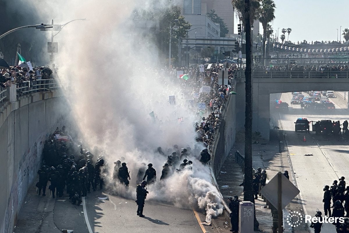 Police officers are enveloped in a cloud of smoke from tear gas and percussion grenades while guarding a highway onramp during a protest against federal immigration sweeps in downtown Los Angeles, California. Photo by Omar Younis