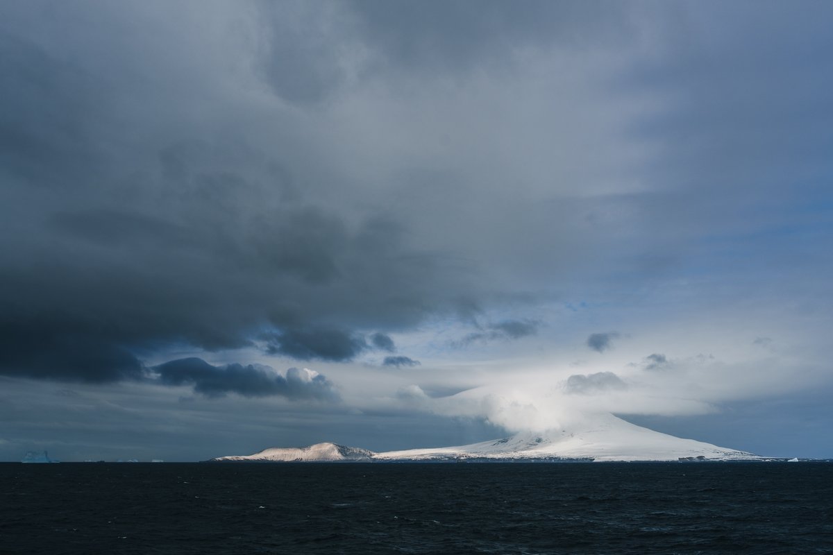 alexinglephoto's tweet photo. W.589 / Saunders Island / South Sandwich Islands

Saunders Island rises from the Southern Ocean like a vision—snow-streaked volcanic slopes, with gas and vapour drifting into stormy skies. Along its blackened shores, vast penguin colonies stand out even from a distance, scattered as flecks of black and white against the land. As the wind howls and waves crash against the coast, giant icebergs drift silently through the storm.