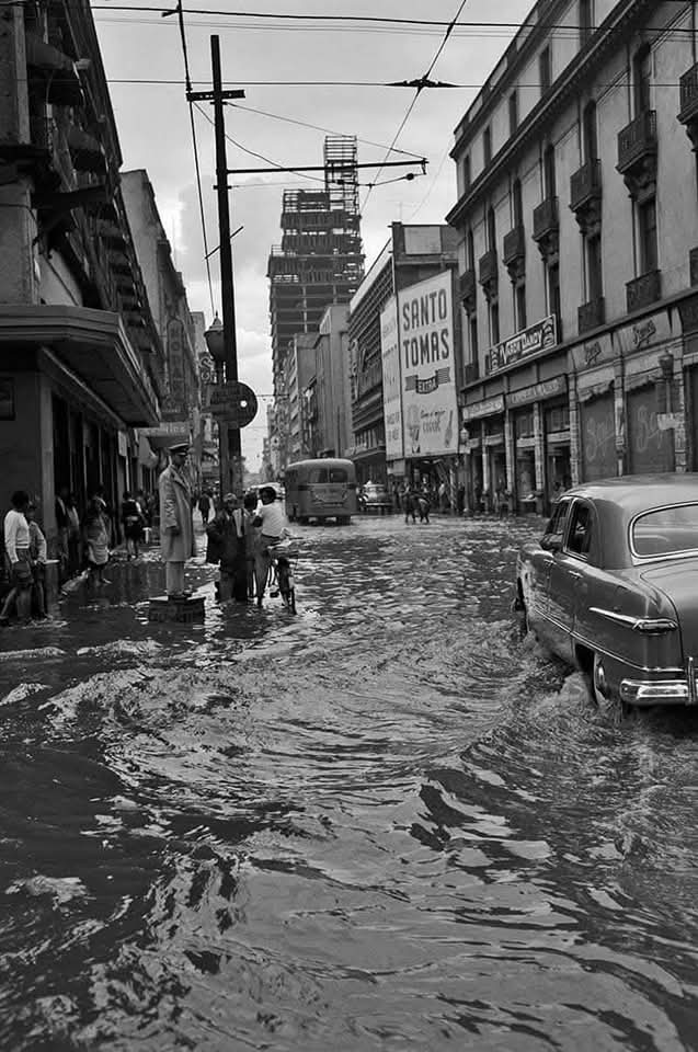 Llueve otra vez en la ciudad, como tantas tardes de junio. Esta imagen de 1952 parece tomada ayer: la calle 16 de Septiembre anegada, un coche clásico detenido en el agua, y al costado, un agente de tránsito firme, casi estoico, desafiando la corriente.