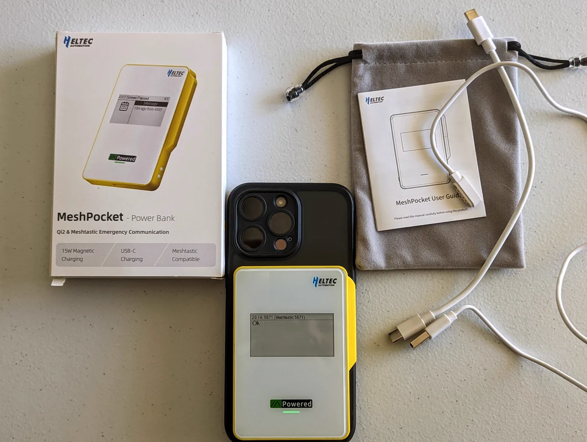 Image shows an iPhone attached magnetically to the Heltec MeshPocket and the contents of the package that are included in the MeshPocket's box including charging cable, data cable with pogo pins to communicate with Meshtastic device, and esp felt bag.