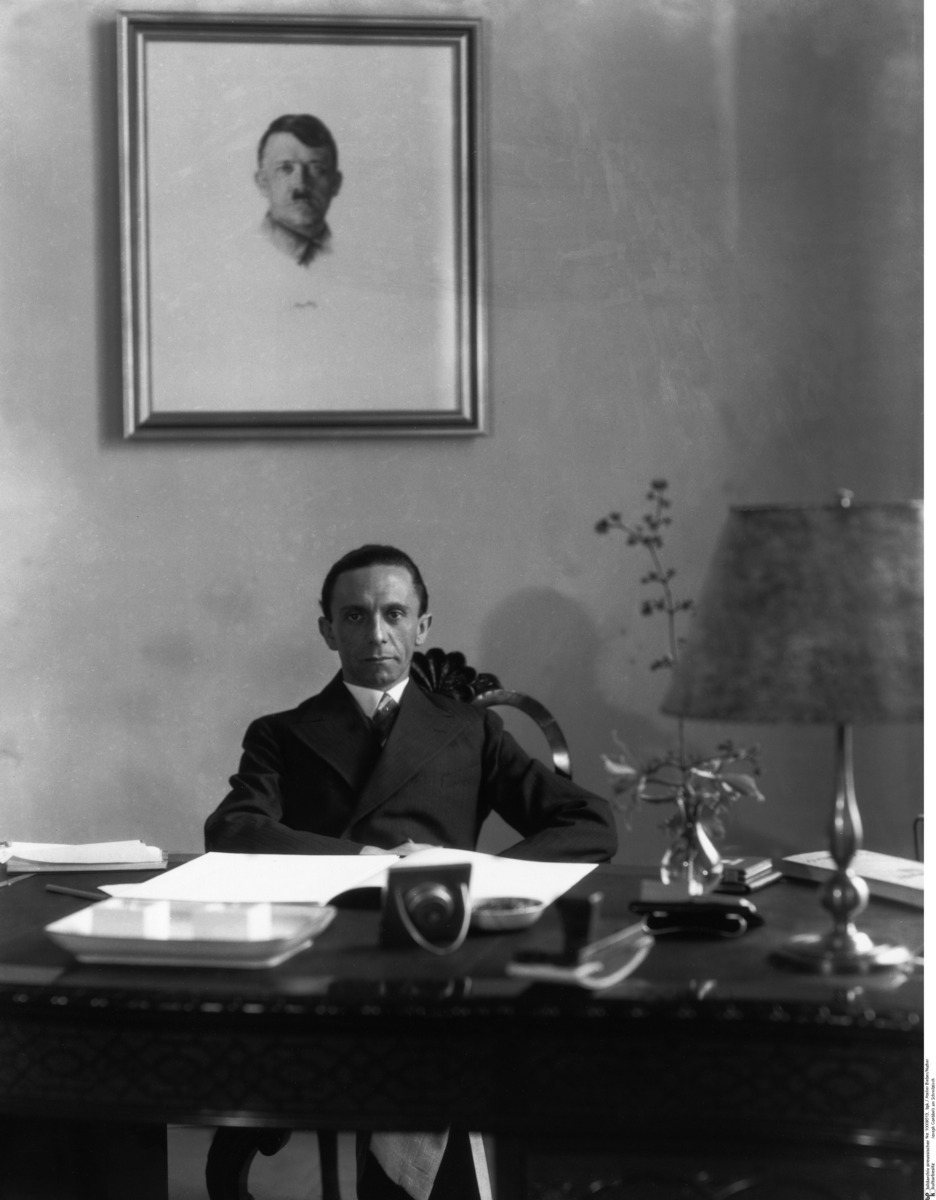 Execution Day....Goebbels Reads the Charges

Goebbels stands in a cold, silent room, the air thick with a stillness that makes every breath feel heavy. The floor beneath his boots echoes with quiet authority. In front of him, a row of government bloggers sits frozen, their eyes