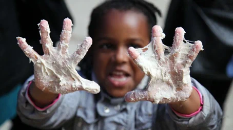 A smiling child holds up their dough-covered hands to the camera