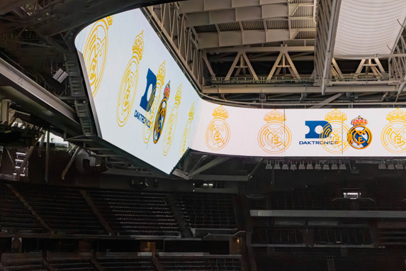 Daktronics's tweet photo. Ever wondered about the tech behind @realmadrid's incredible new halo display at Santiago Bernabéu Stadium? We sat down with Enrique, the club’s head of IT. If you haven't listened to our podcast episode, or you prefer to read, this one's for you! https://t.co/XPCPbScEos #DakPro https://t.co/fvYzLGulRr
