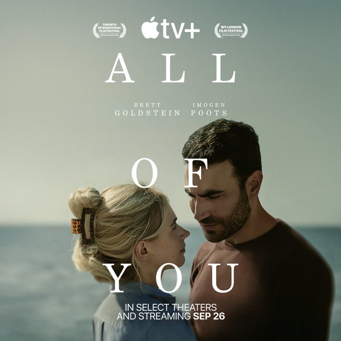 From All of You. Standing against a backdrop of the ocean, Brett Goldstein looks down into Imogen Poot's eyes. He wears a brown t-shirt while she has on a chambray button-down with her hair up in a claw clip. At the top of the image there are three separate logos for Toronto International Film Festival Official Selection, the Apple TV+ one and the BFI London Film Festival Official Selection all in line with each other. Starting in the center of the image, the title All of You is stacked with Brett Goldstein and Imogen Poot’s names under the word all. At the bottom of the image the words, in select theaters and streaming Sep 26 is written.
