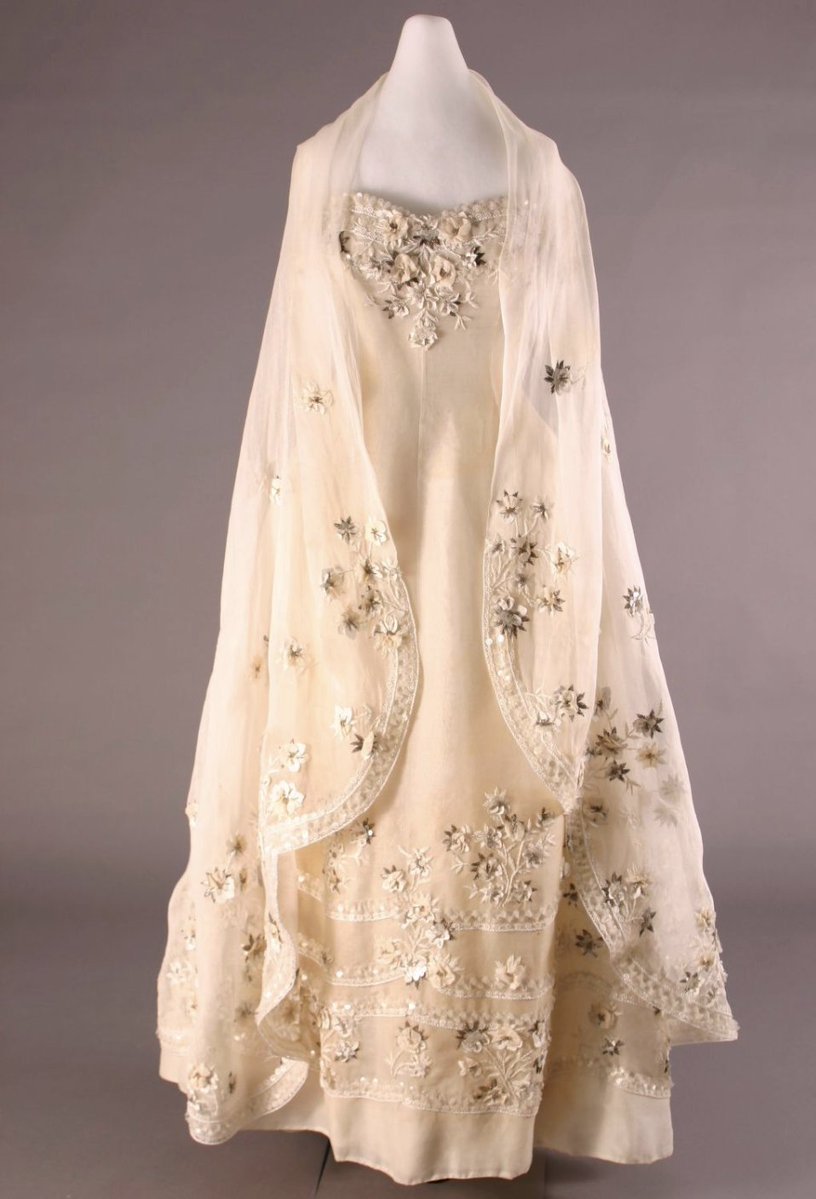 bowjtl's tweet photo. is this 1955 Dior evening dress with a stole, made of white cotton organza over layers of nylon. The floral embroidery is incredible various materials- white raffia, silver thread, silver beads, white horsehair, pearl-like sequins, and silk flower petals https://t.co/81gPoGuNRo
