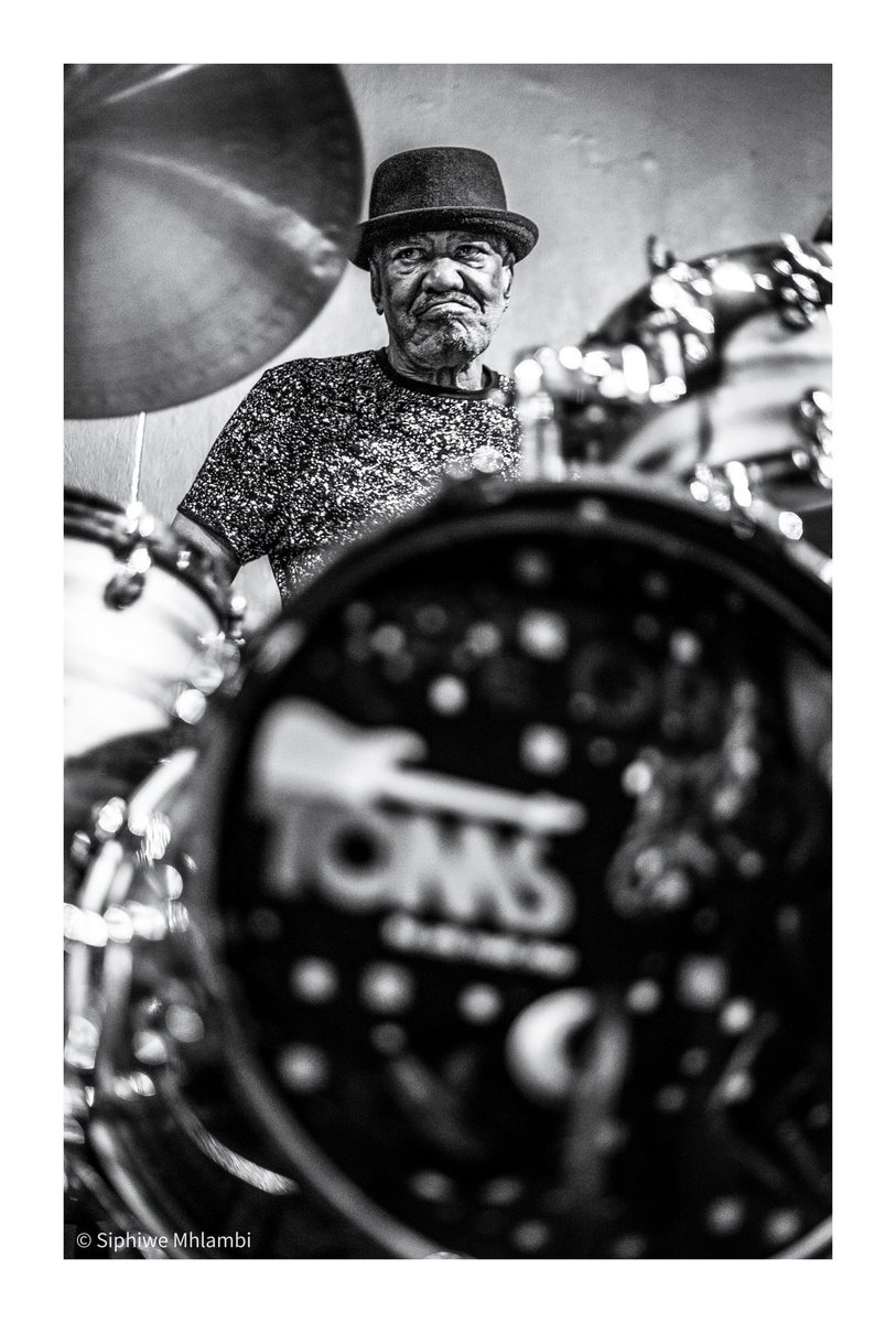 Yes, baby. No baby
Vukile Pokwana
A Tribute to Louis Moholo-Moholo
The cymbals speak in tongues of flame,
A whisper, a wail — not bound by name.
In sound’s rebellion, wild and free,
You lit the path for what could be.
Yes, baby. No baby.
From Langa’s dust to London’s grey,
Your