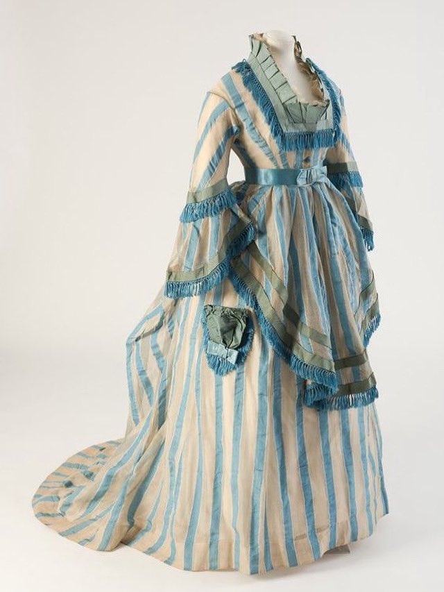 kateStrasdin's tweet photo. There is a vaguely seaside theme to this busy mid #1870s gown, deckchair stripes and sea blue trim a cheery combination. I wonder if it was a promenade dress for some beach front strolling? @Fashion_Museum #fashionhistory https://t.co/8OTzUFDlP5